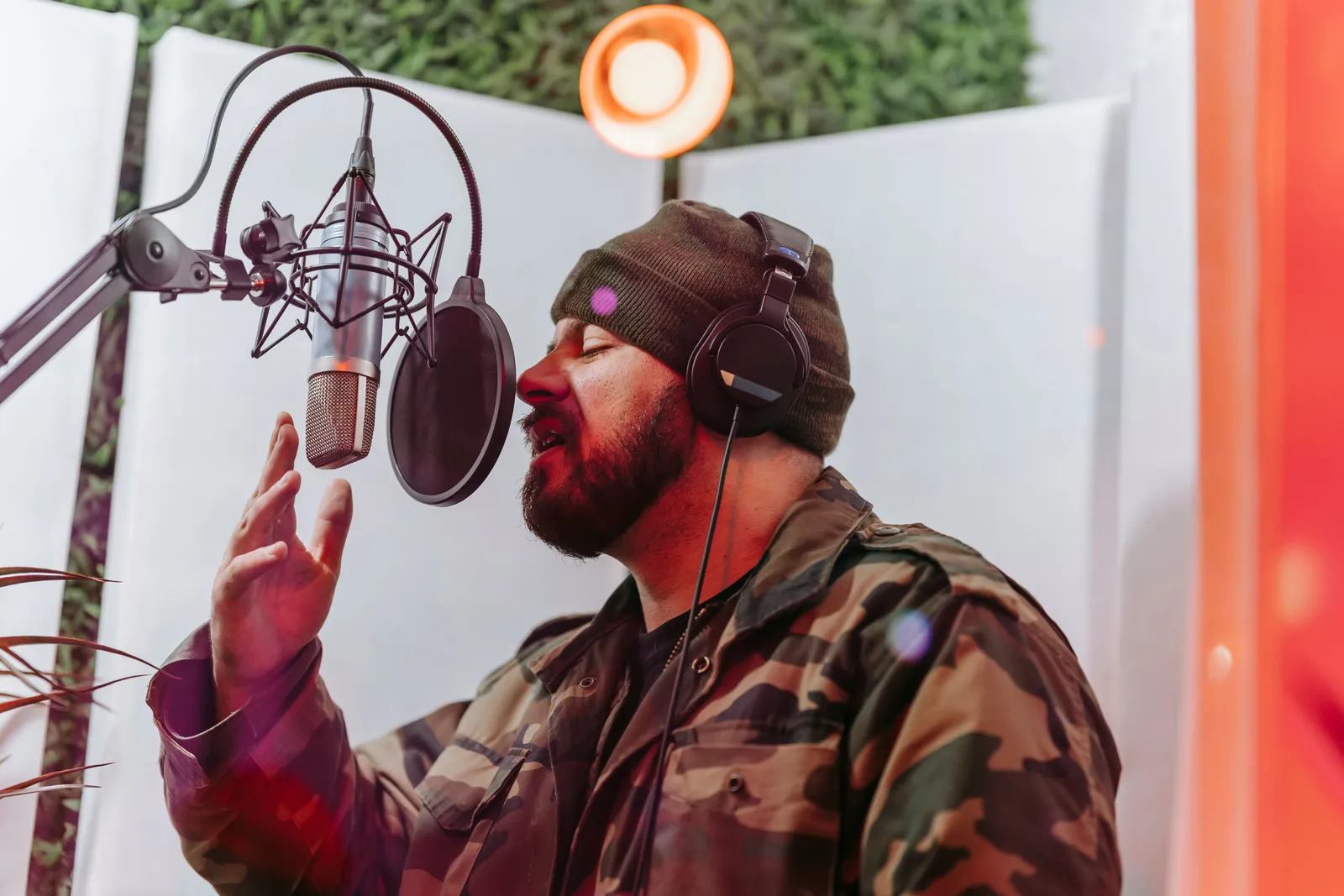 Male musician in recording studio singing into a microphone, wearing headphones and camouflage jacket