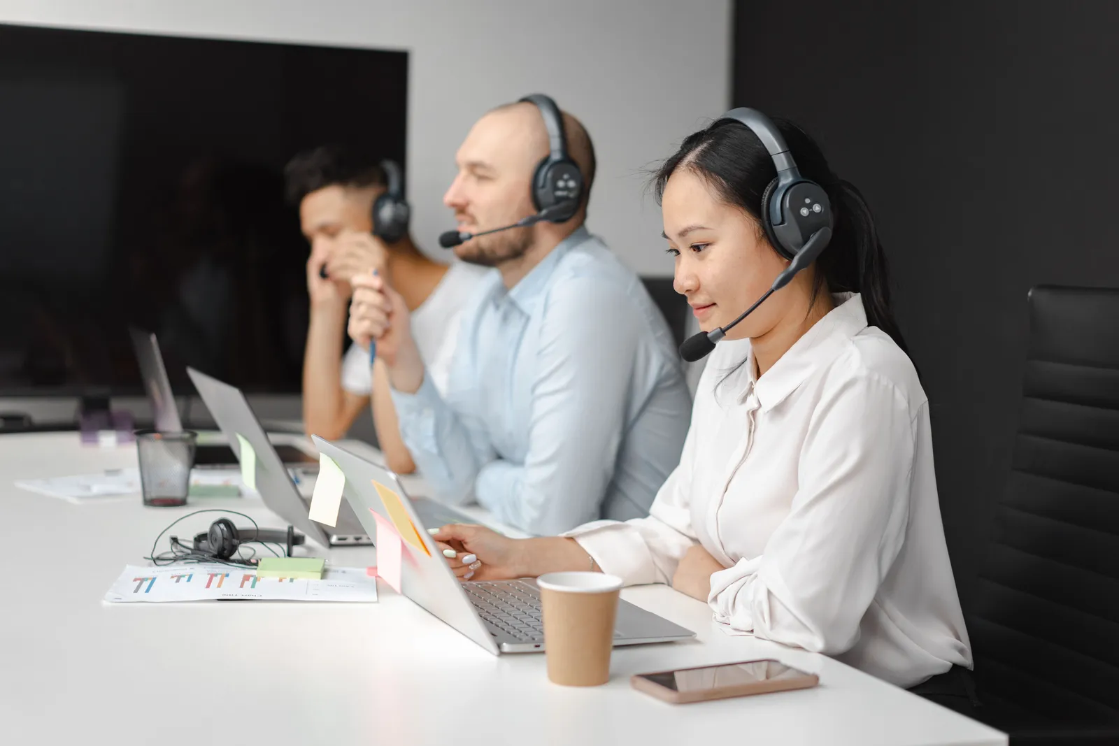 Call center agents wearing headsets working on laptops at a customer support team meeting