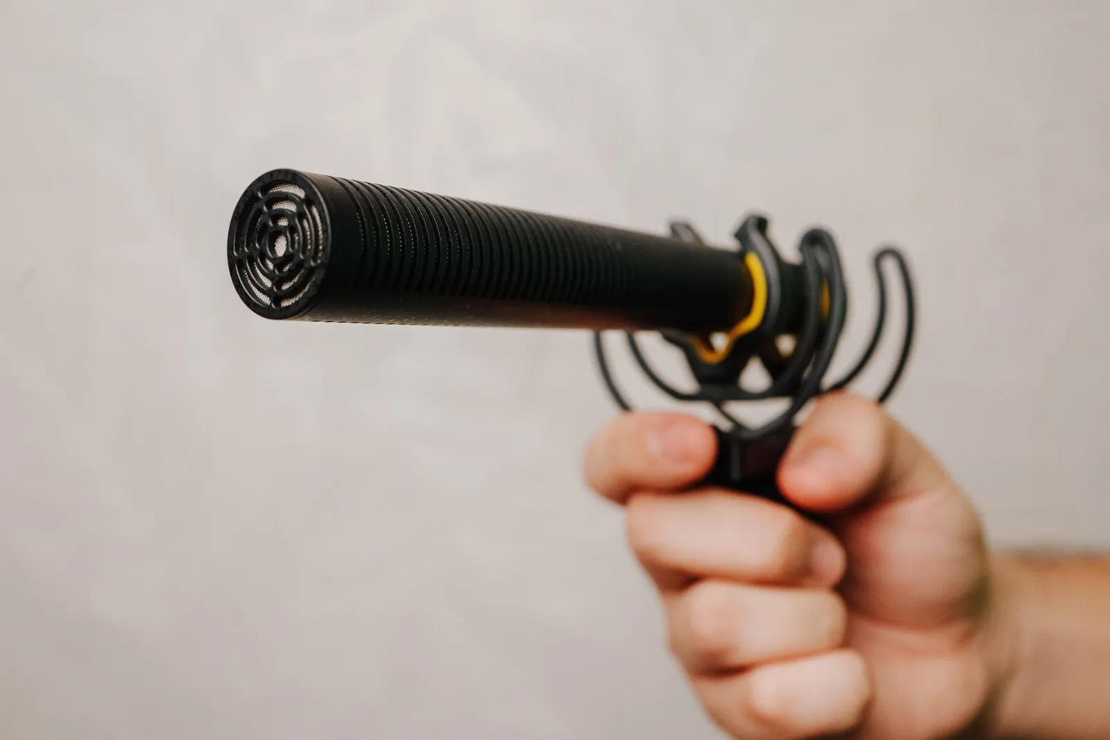 Hand holding a shotgun microphone with foam cover, ideal for voice recording and audio capture