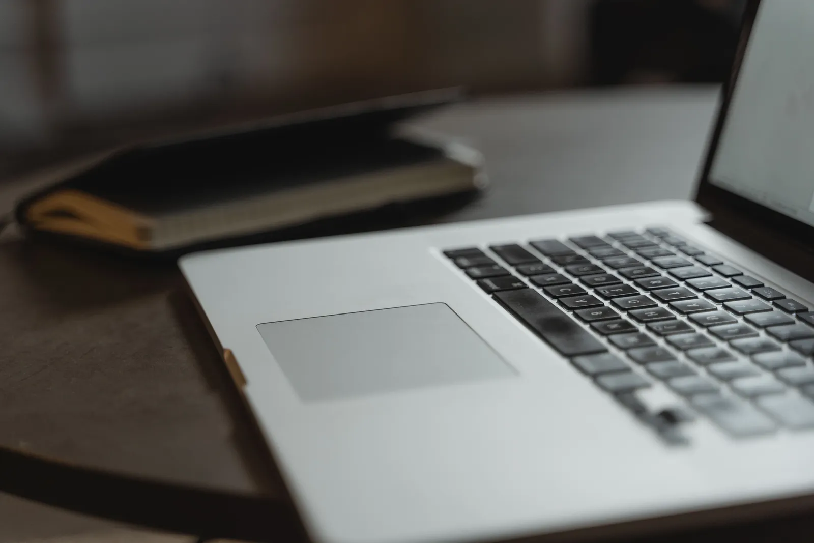 Close-up of a laptop keyboard on a desk with a notebook in soft focus