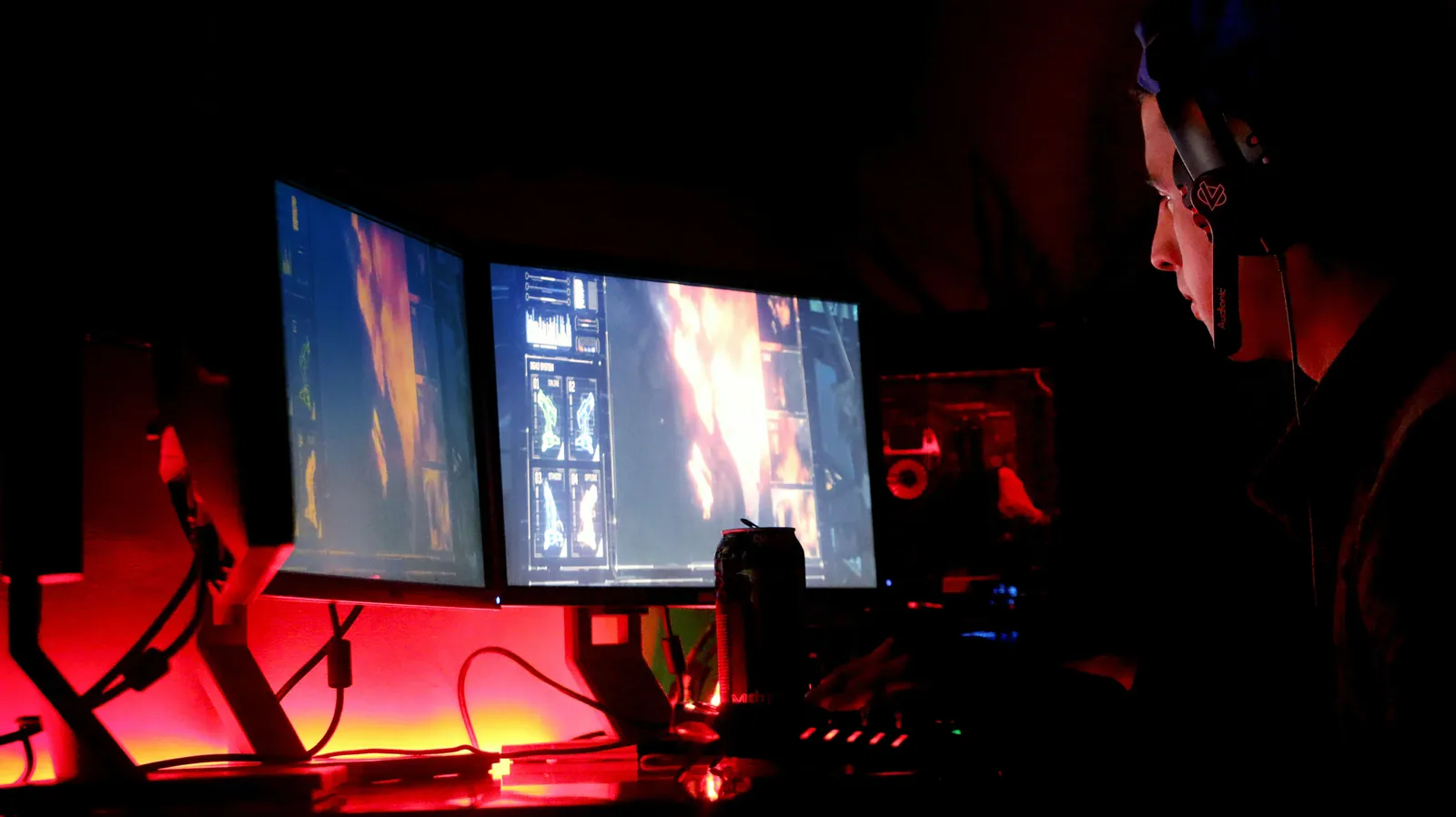 A man intensely focused on multiple computer monitors in a dimly lit room, illustrating high-tech work environment