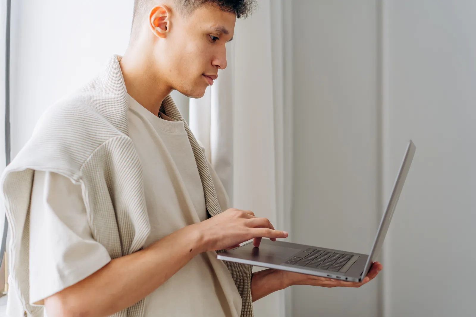 Stylish young man using a laptop indoors, focused on the screen during the day