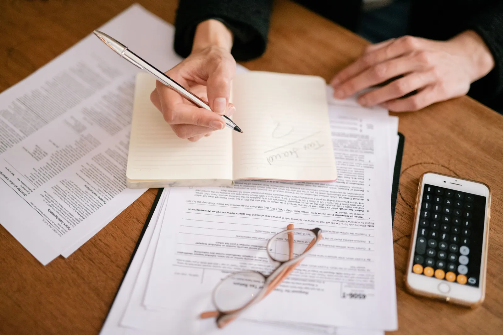 Close-up of a person writing in a notebook with documents and a calculator, managing finances