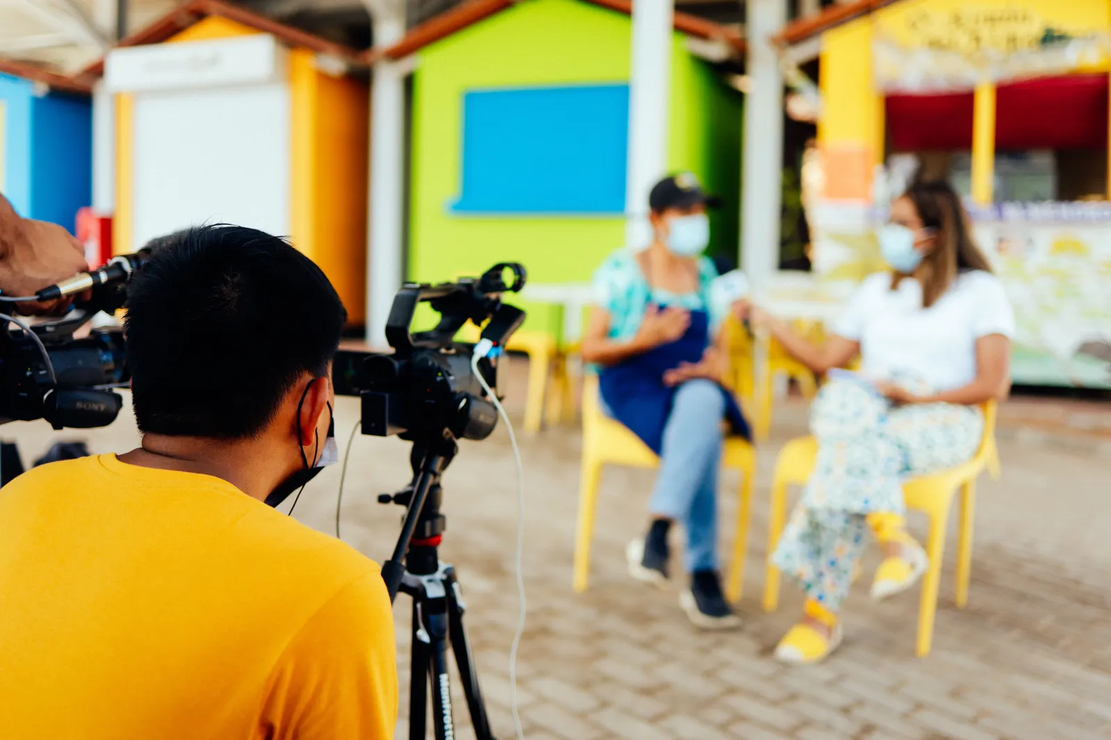 Camera crew filming an outdoor interview with masked participants for a documentary