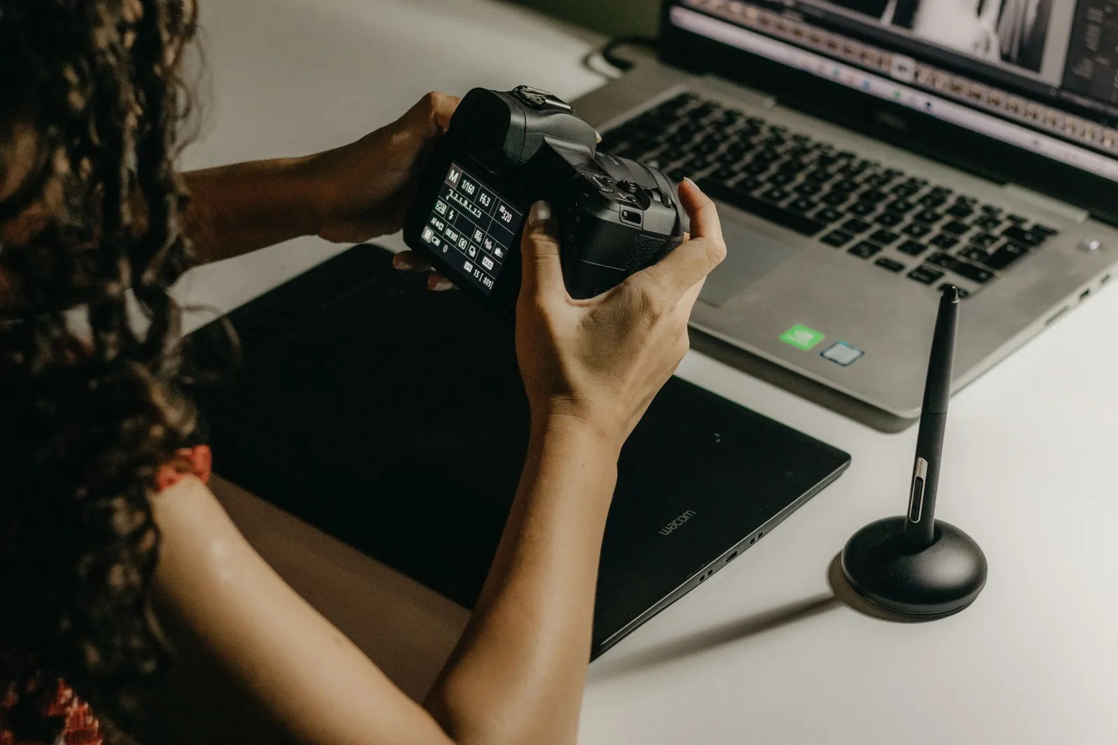 A woman reviews and edits her photos using a camera and laptop at a desk