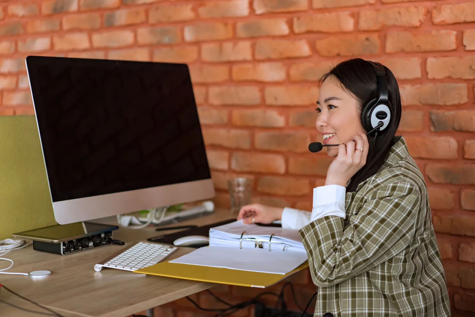 Smiling female call center agent working at desk with computer and headset