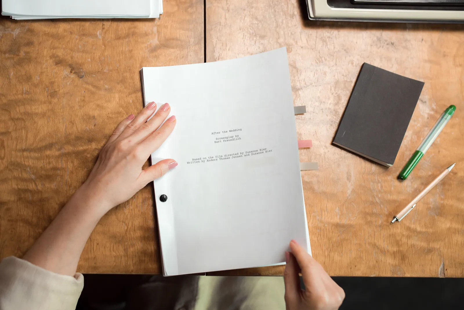 Close-up of hands organizing documents on a wooden desk with pen and notebook