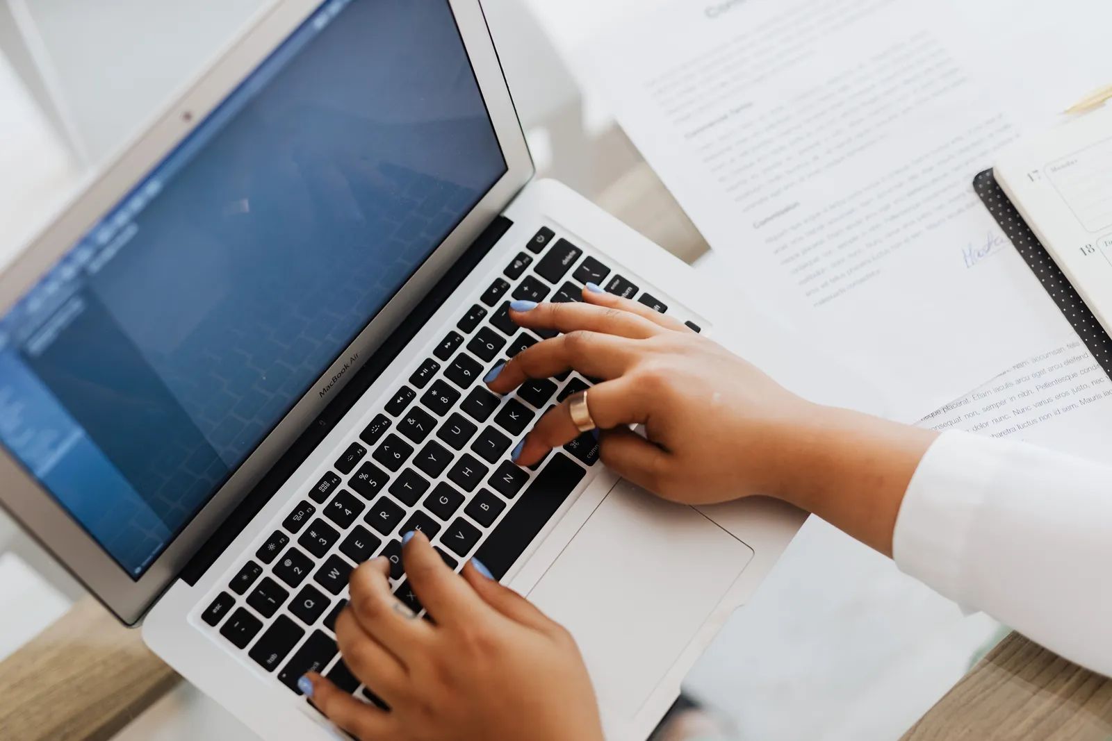 Close-up of hands typing on a laptop surrounded by papers, showcasing modern work setup