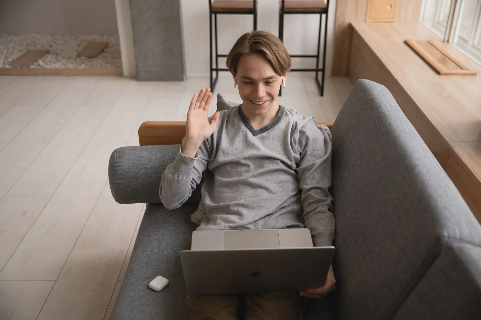 Smiling young man waving during a video call while using a laptop at home