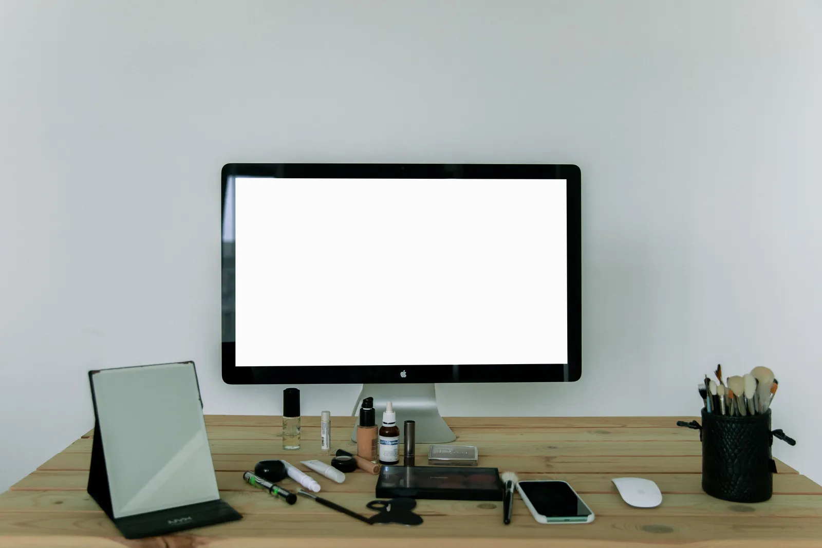 A neatly arranged desk with a computer screen, makeup tools, and mirror, perfect for modern workspaces