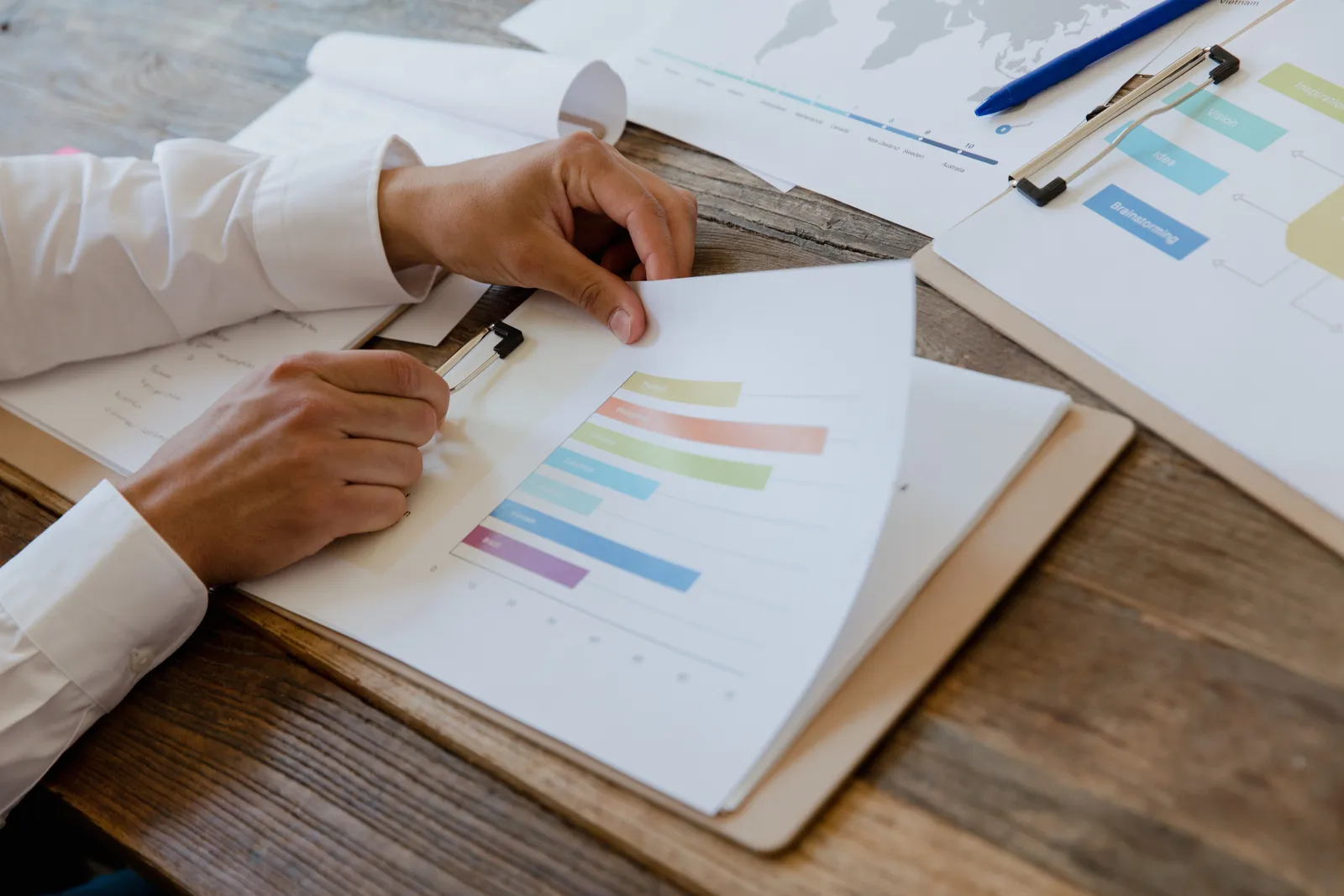 Close-up of hands reviewing business report with colorful charts and graphs on a wooden desk