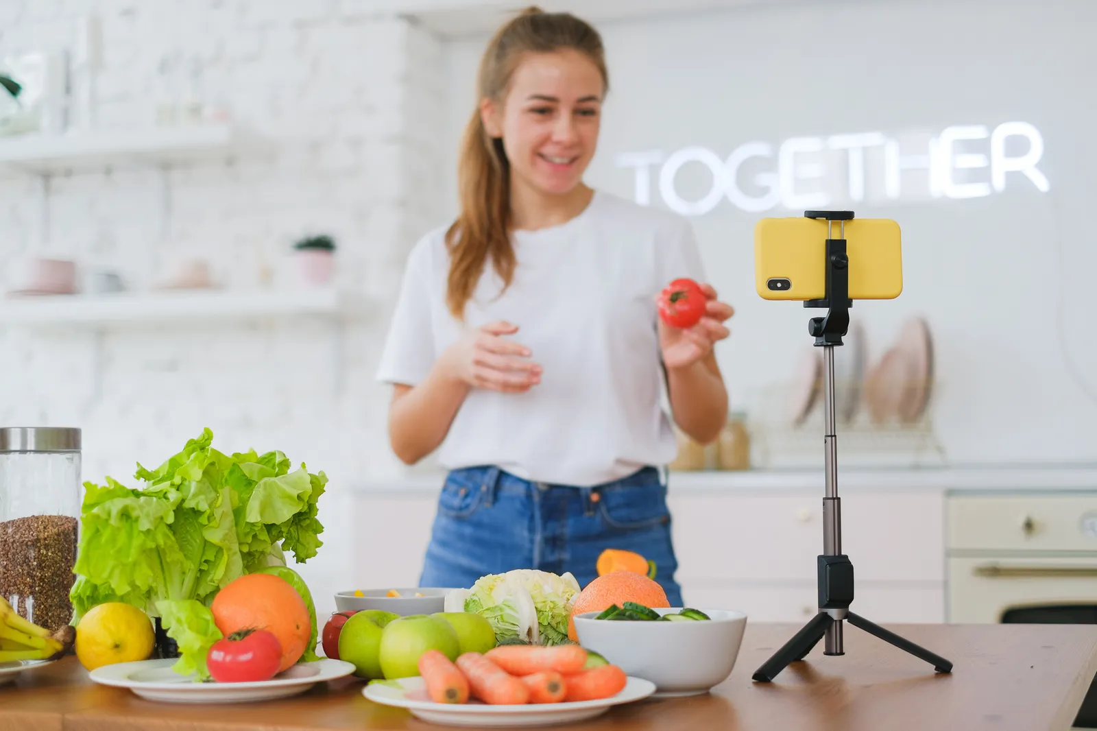 Young woman filming a healthy cooking video in a bright modern kitchen with fresh vegetables