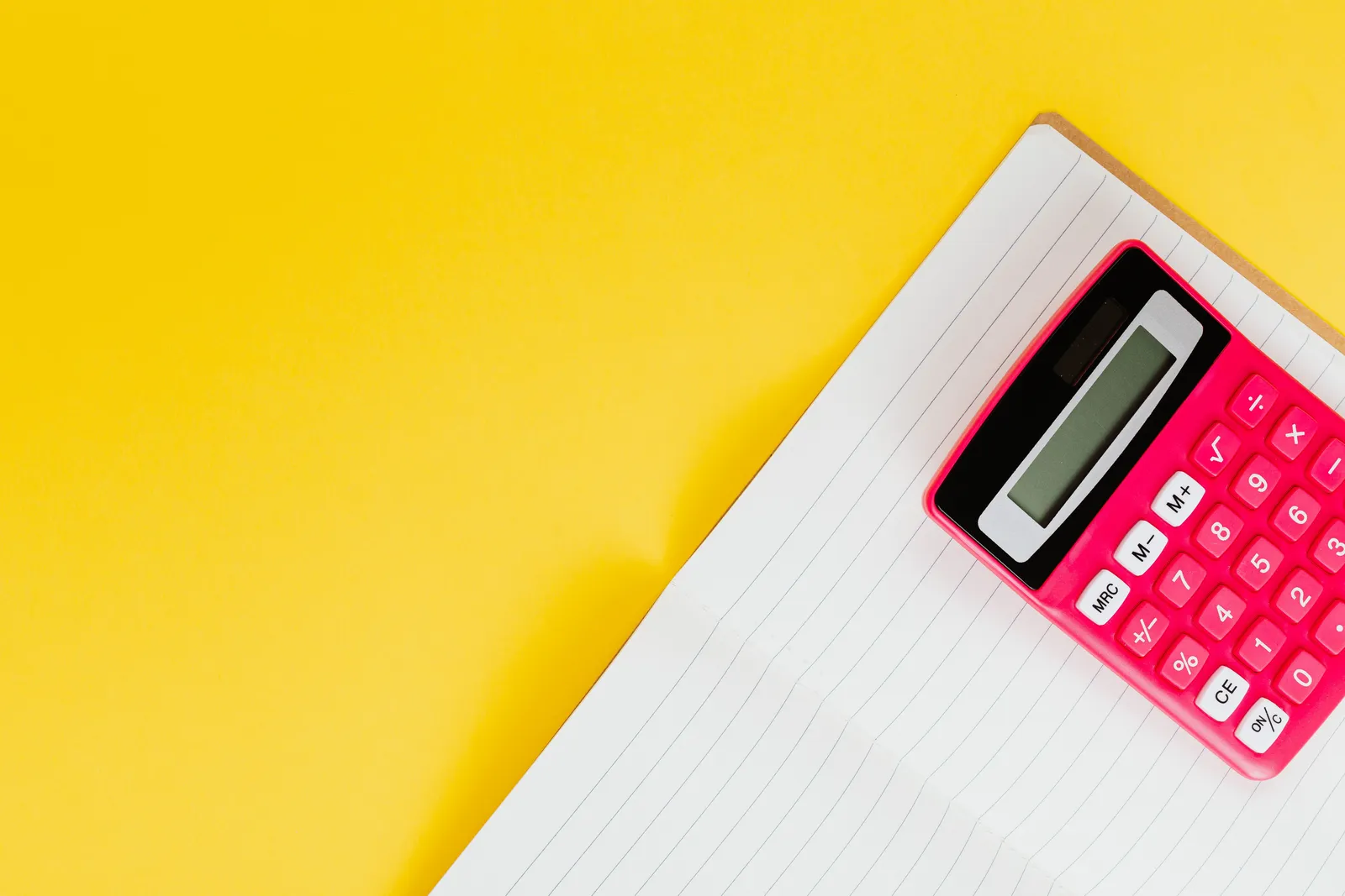 A vibrant pink calculator placed on a lined notebook against a bright yellow surface, showcasing office or school tools
