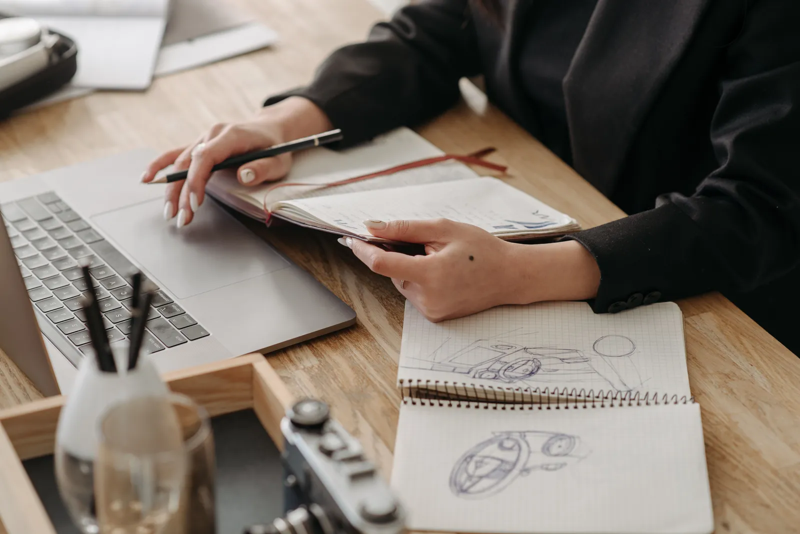 Desk with a laptop, sketches, and hands holding a notebook, embodying creative work