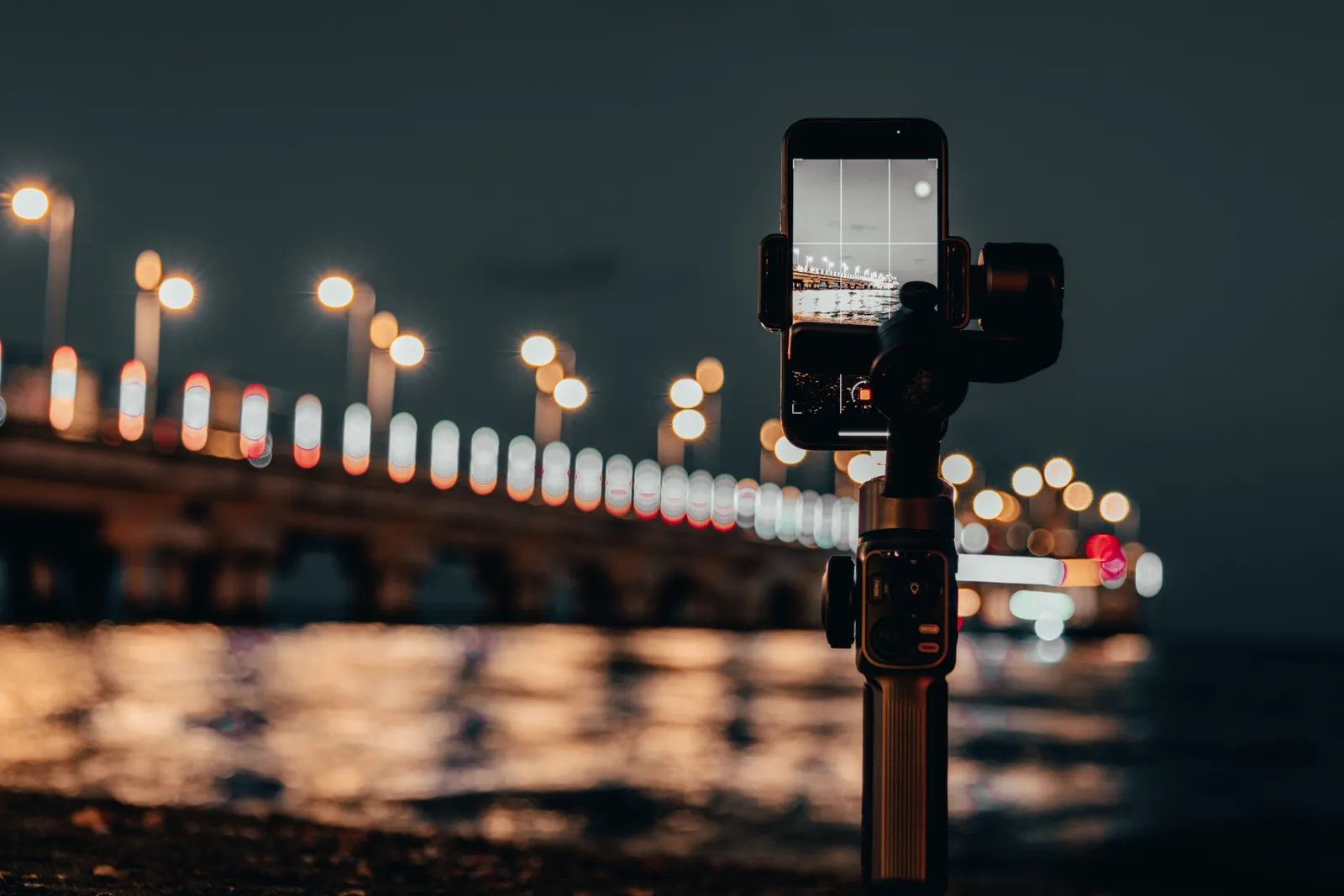 Captivating night scene capturing a smartphone on a tripod filming Ănye pier with bokeh lights in the background