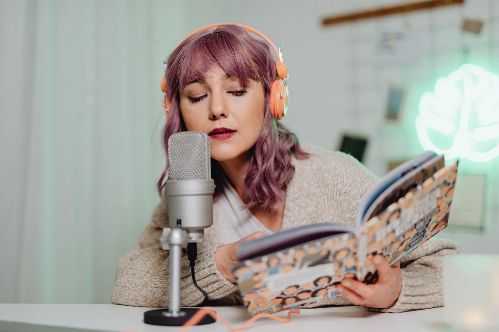 Woman with headphones reading a book into a microphone indoors