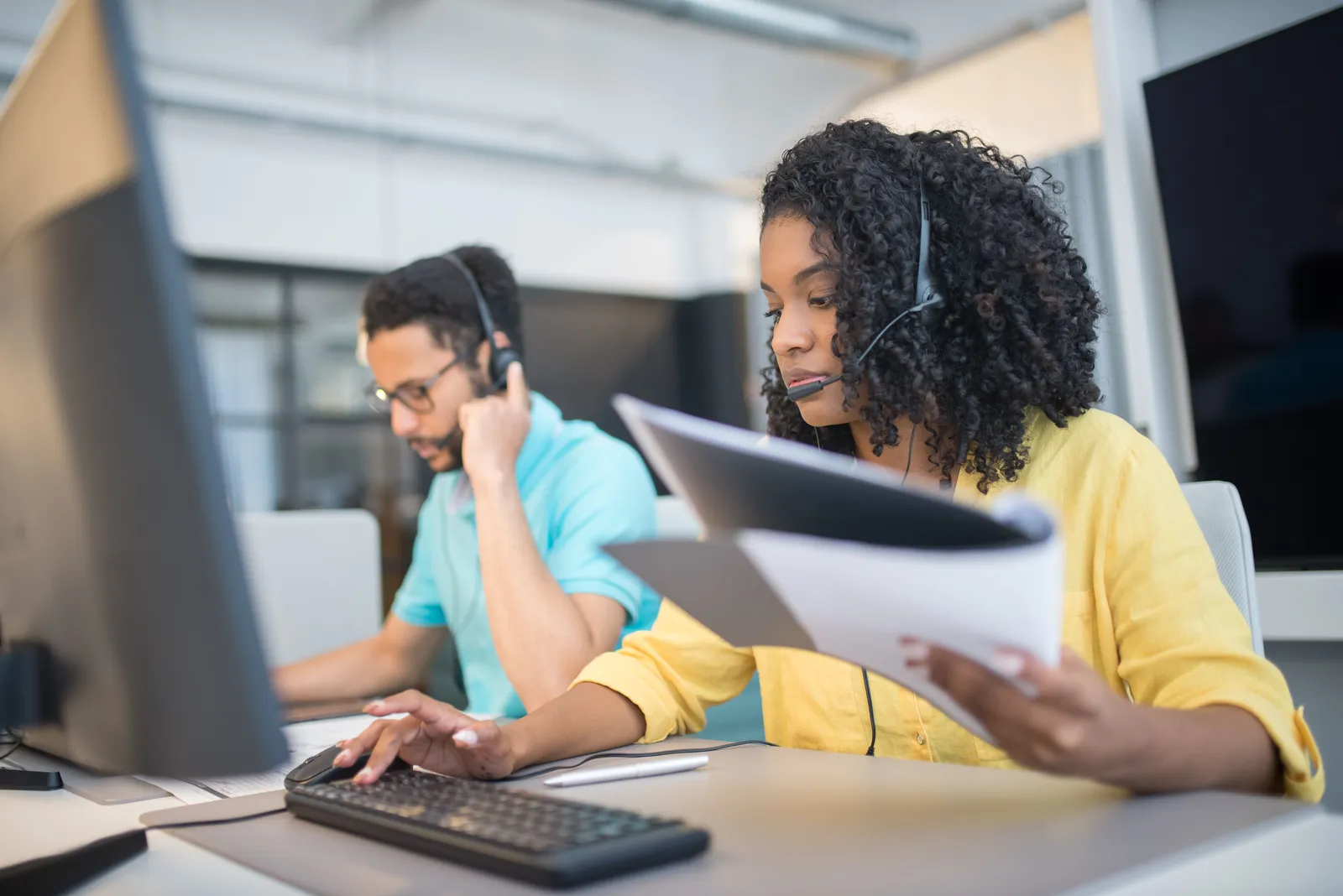 Two customer service representatives working with headsets in a modern office setting