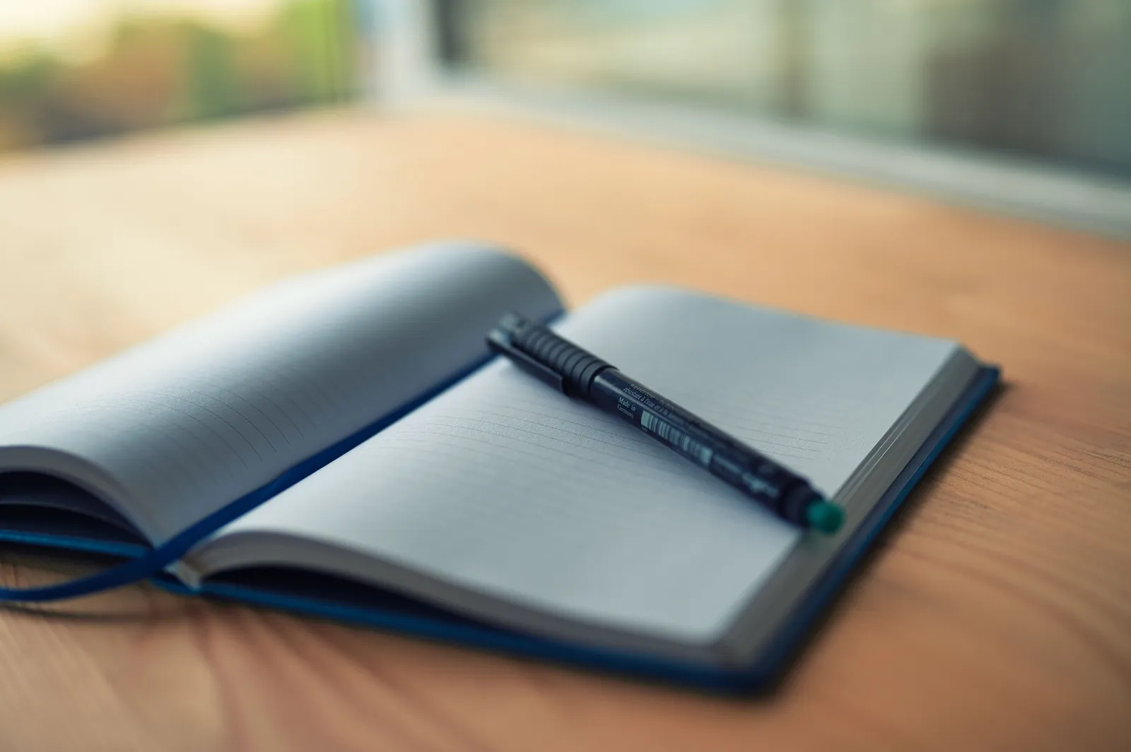 An open lined notebook with a pen resting on a wooden desk, capturing a moment of creativity