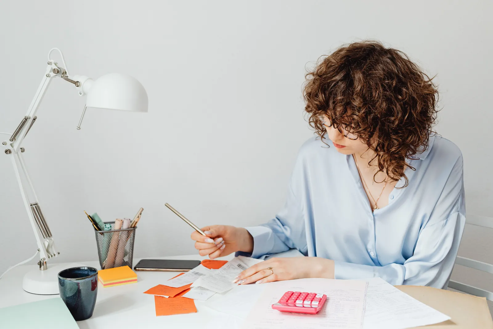 Woman in office calculating expenses with documents, calculator, and coffee