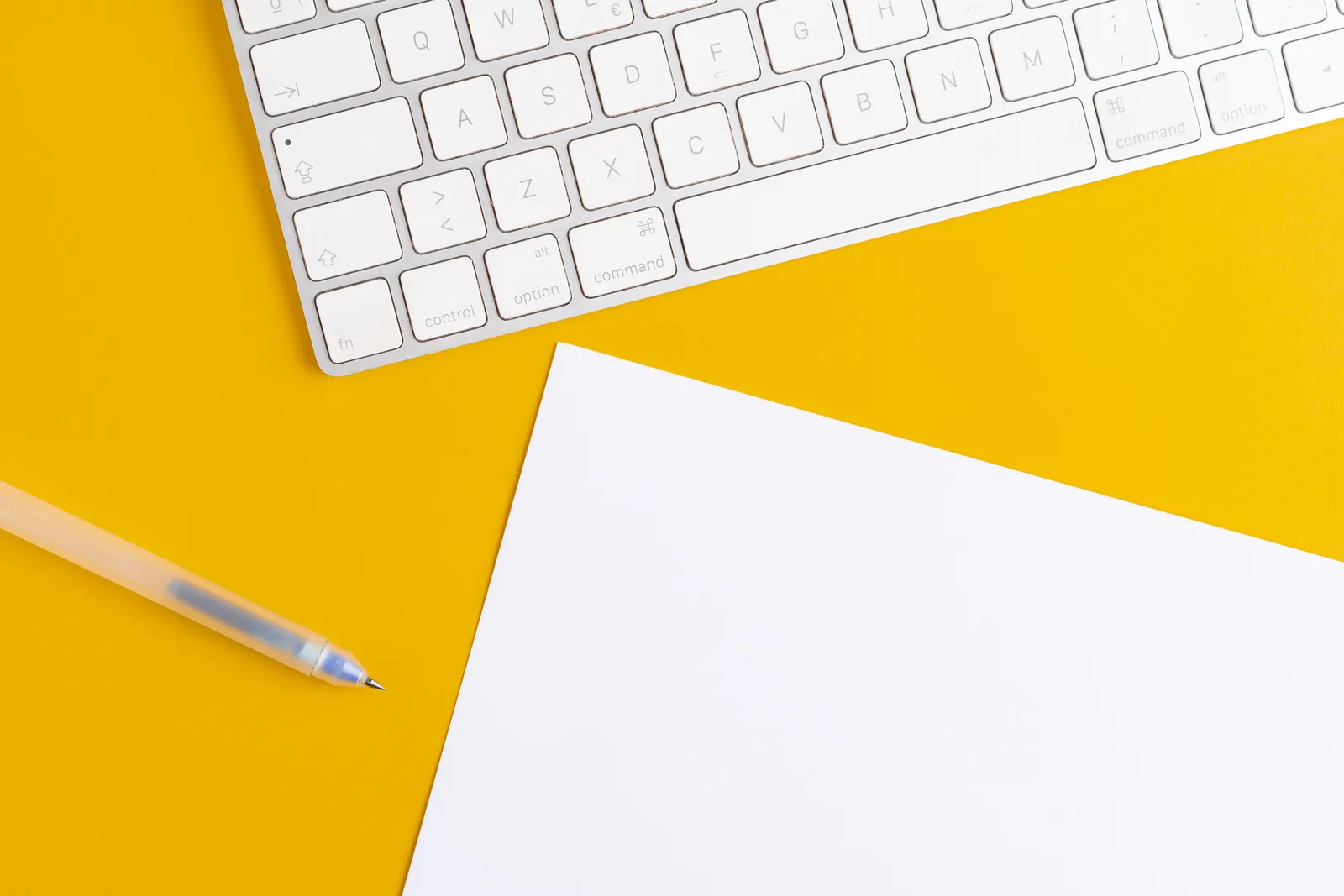 A minimalist office setup with a keyboard, pen, and paper on a vibrant yellow background