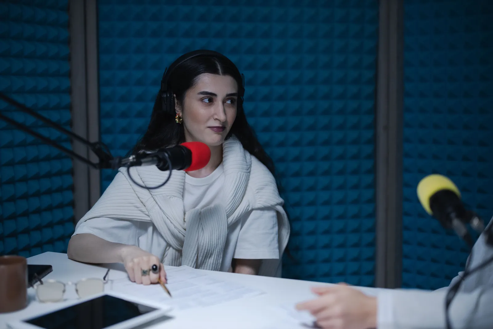 A woman in a podcast studio with microphones and headphones, focused on a discussion