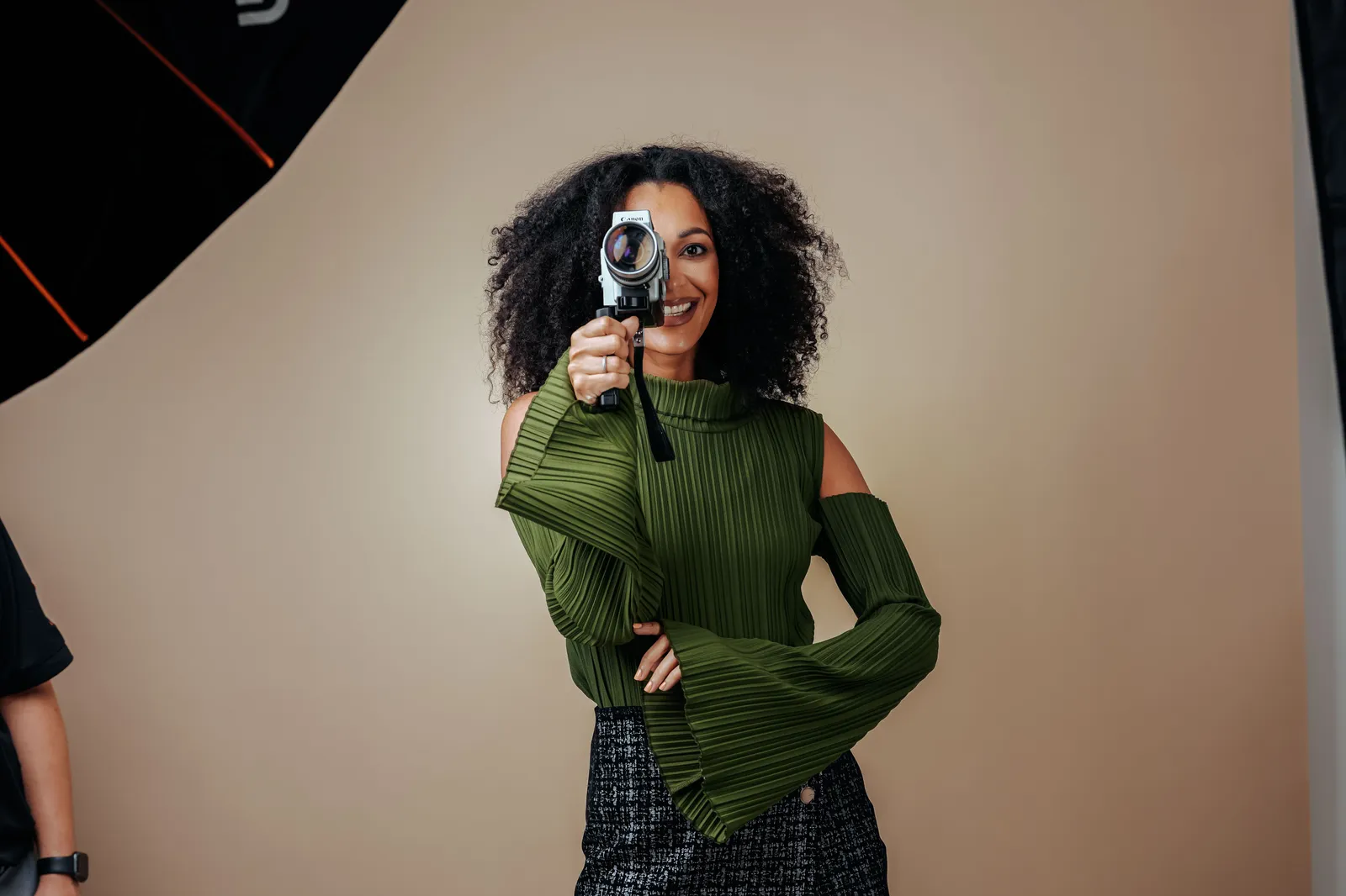 Woman in green sweater posing with a vintage camera in a photo studio