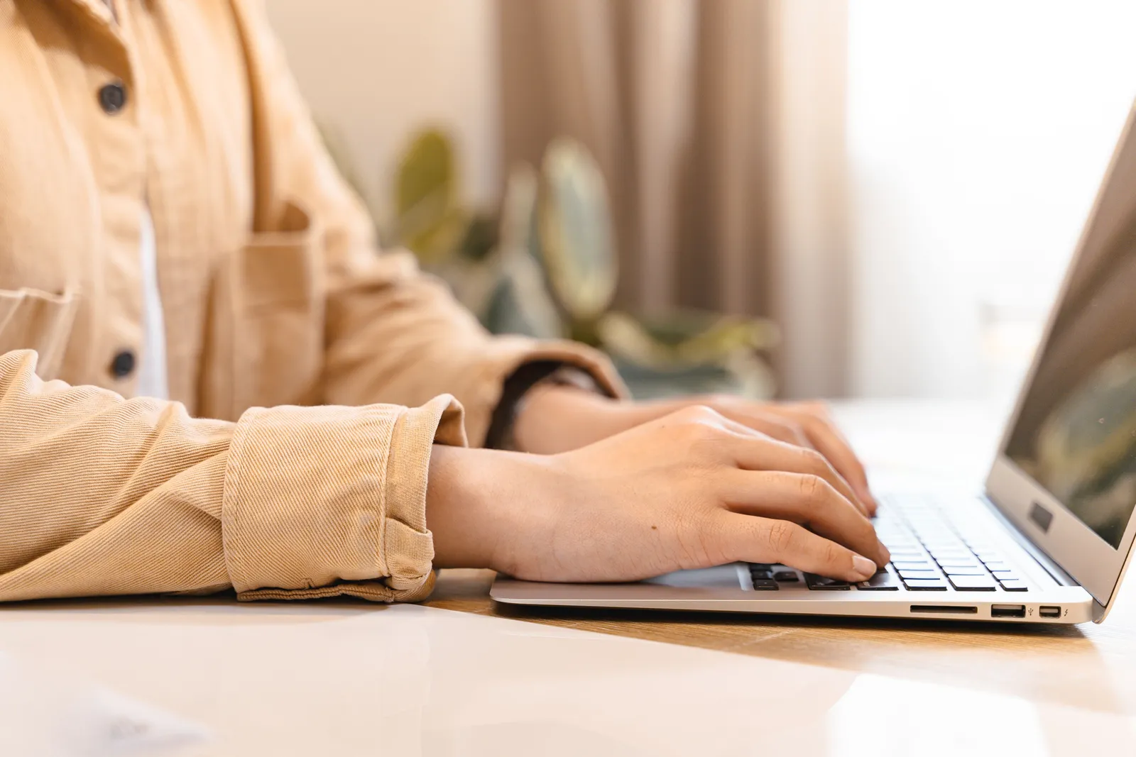 Close-up of hands typing on a laptop indoors, wearing a casual jacket