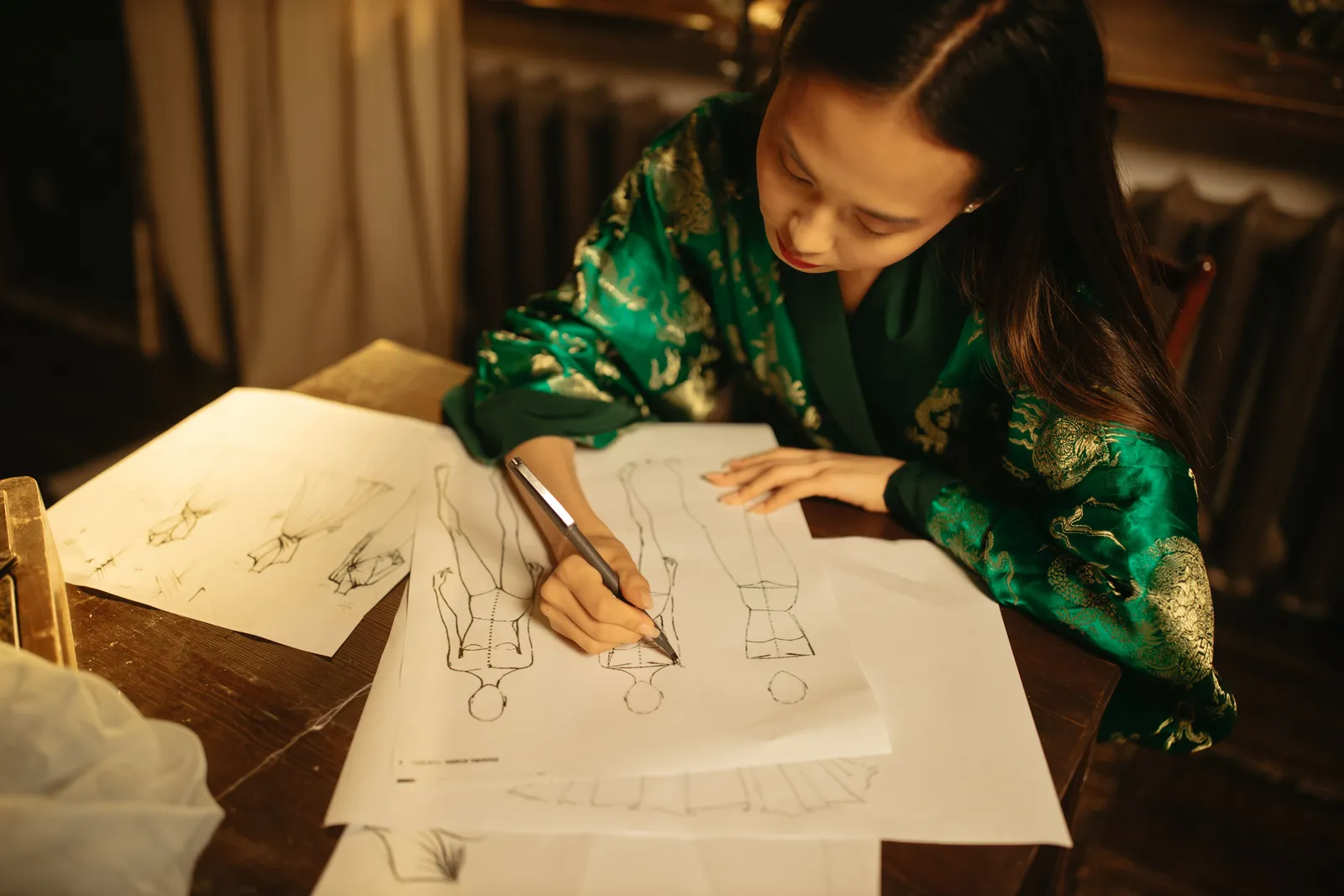 Woman fashion designer sketching clothing designs at desk, showcasing creativity and concentration