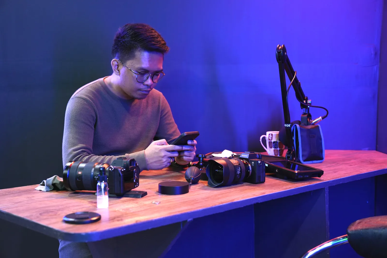 Man sitting at a desk with cameras and microphone, using smartphone