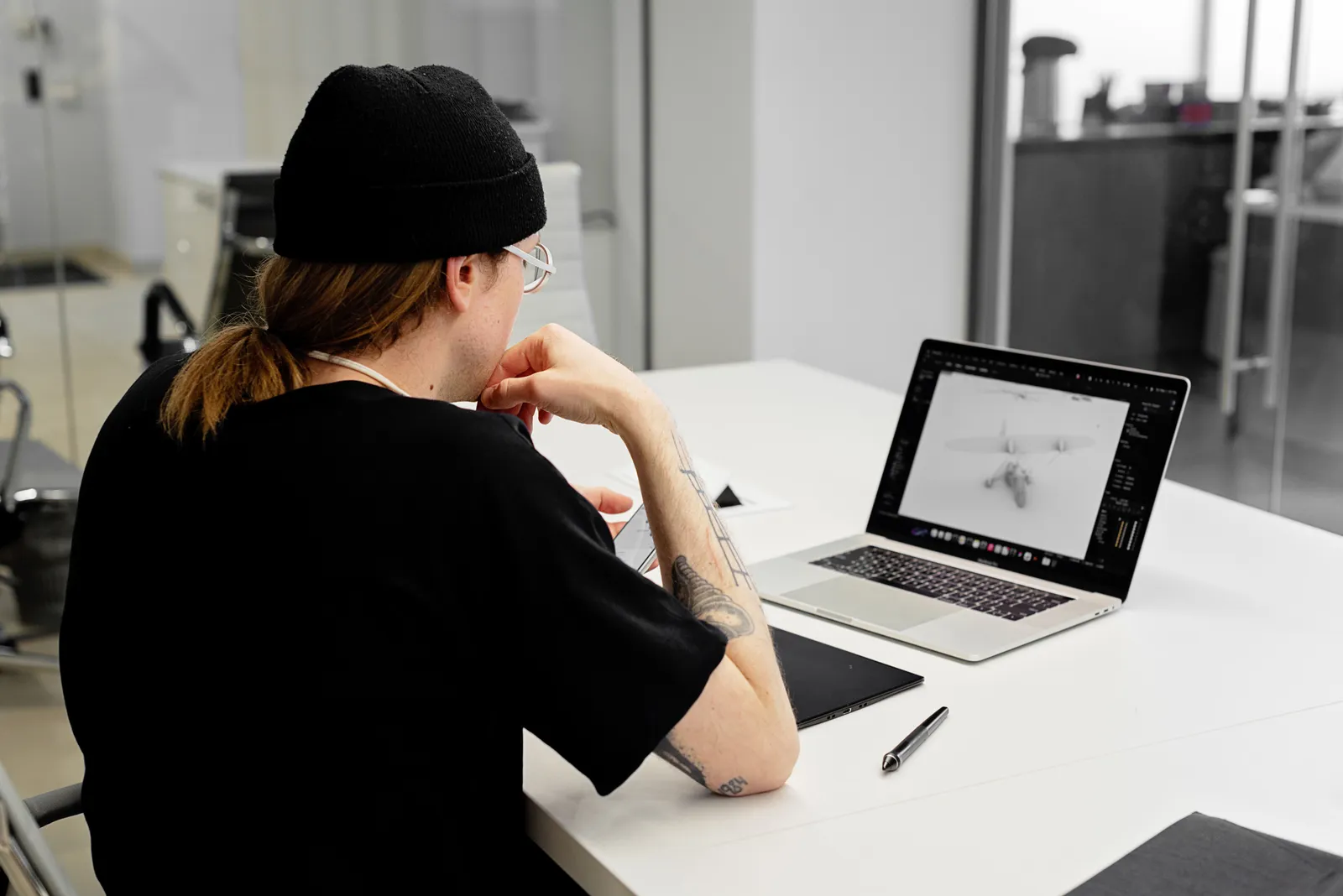 A focused designer in a beanie works on a laptop in a modern office
