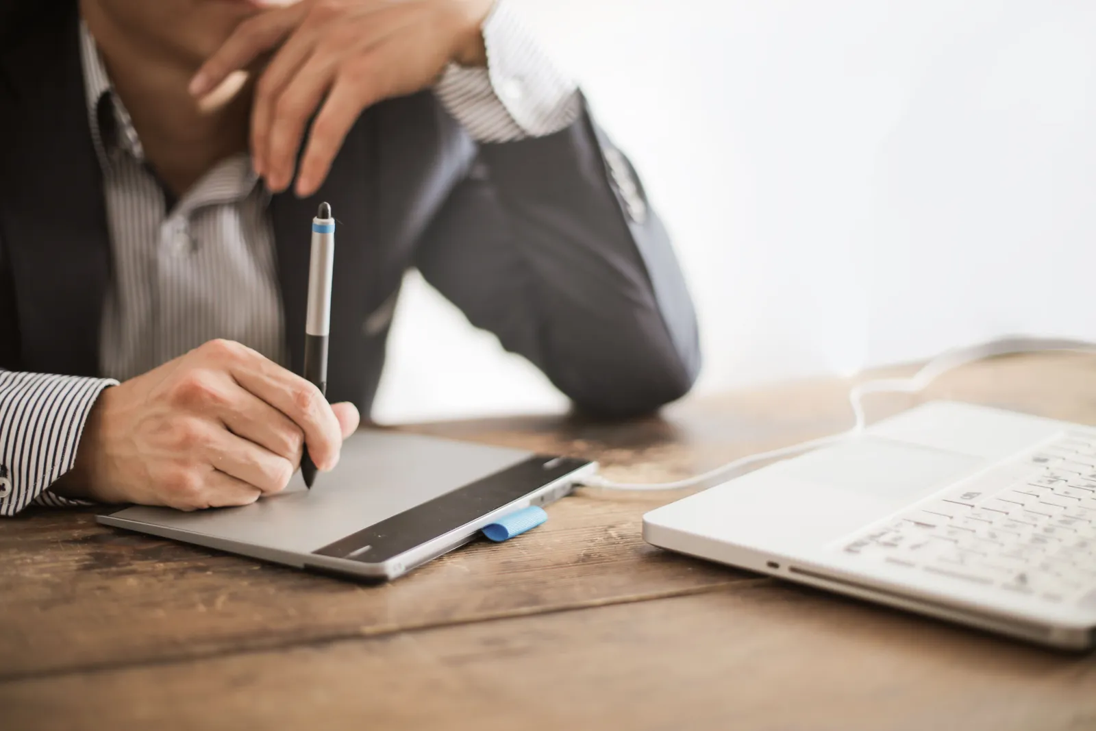Crop elegant man watching laptop while drawing on graphic tablet at wooden desk