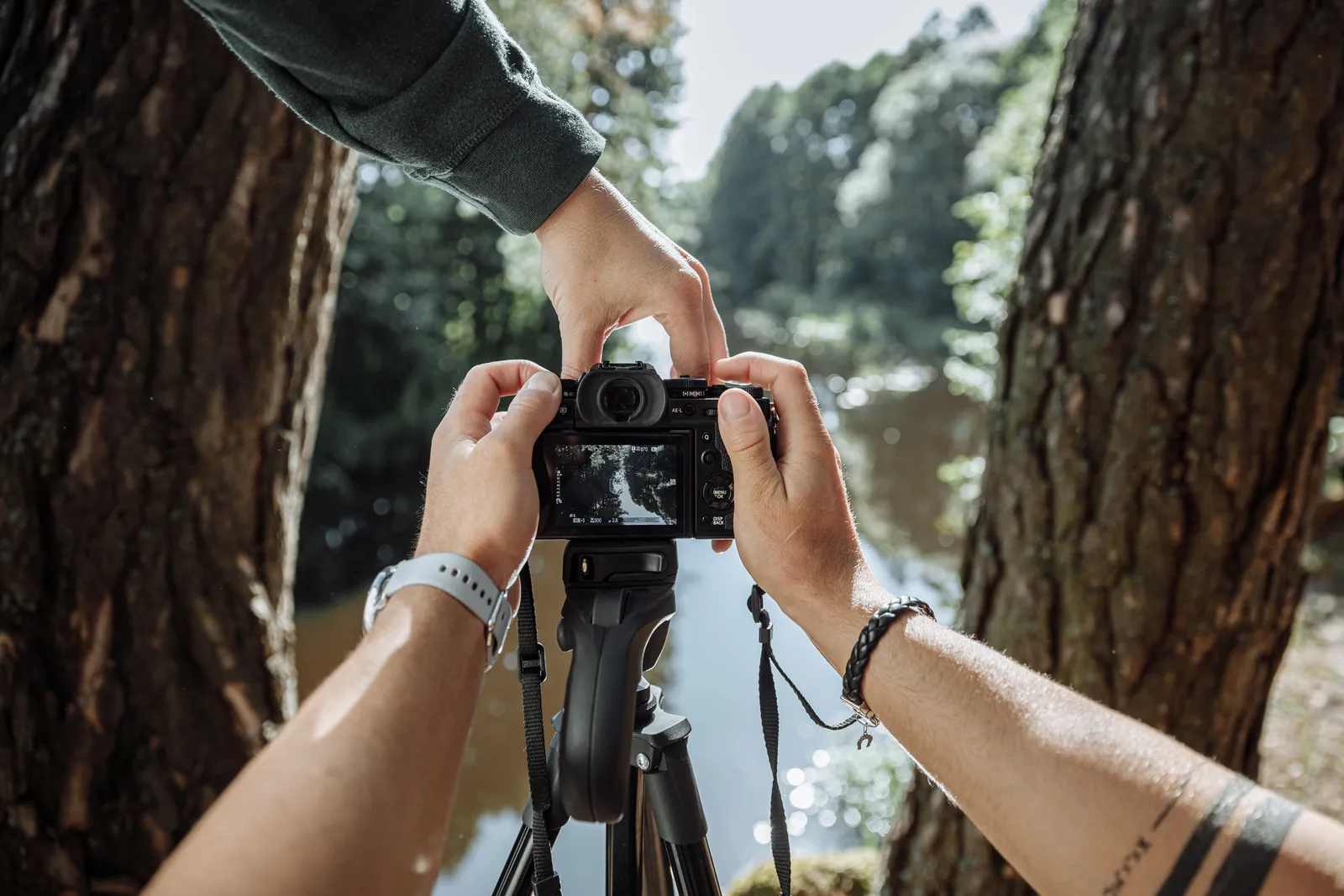 Close-up of hands setting up a camera on a tripod near a scenic forest river