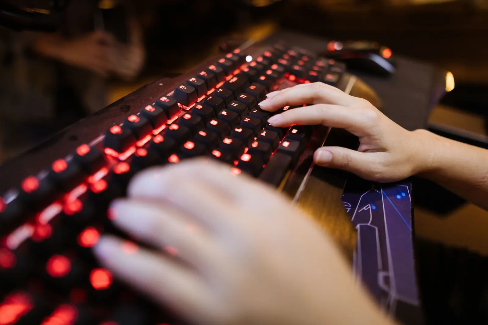 Focused shot of hands typing on a glowing mechanical keyboard in a dimly lit room