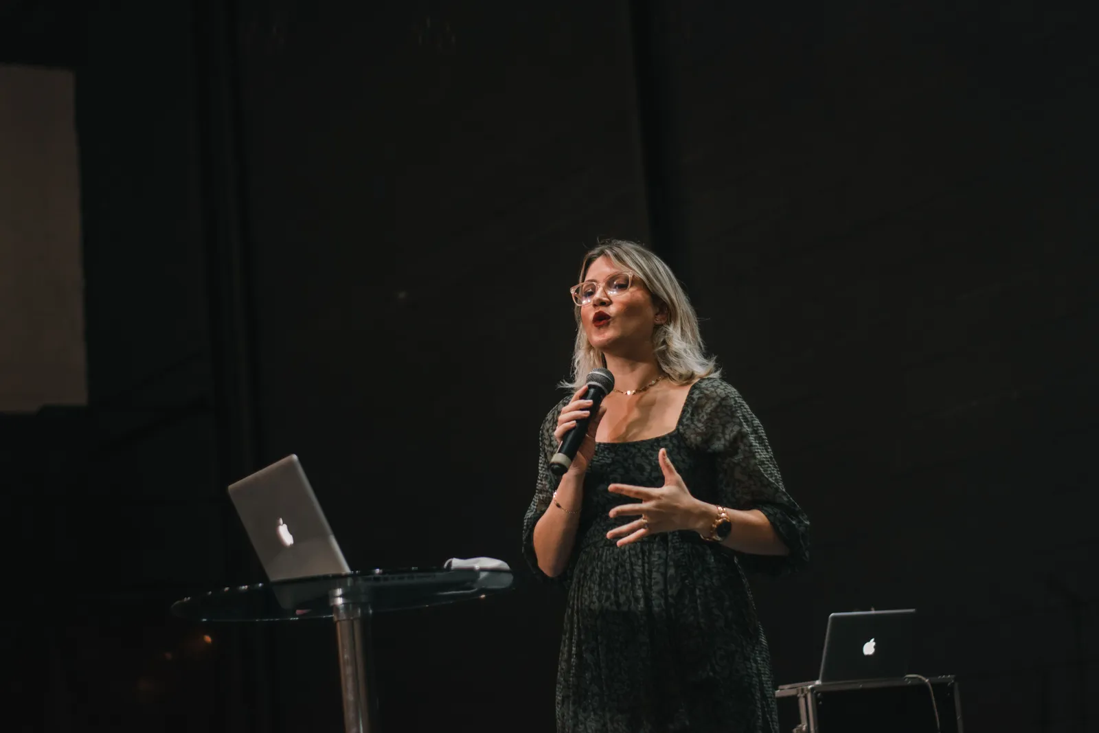 A confident woman delivers a speech on stage with a microphone and laptop