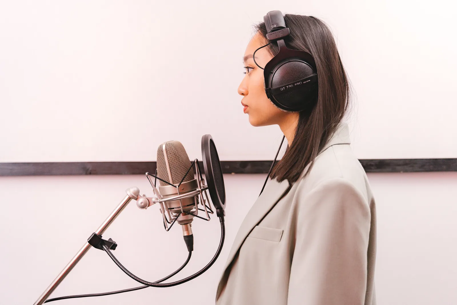 Side view of an woman with headphones singing into a condenser microphone in a studio