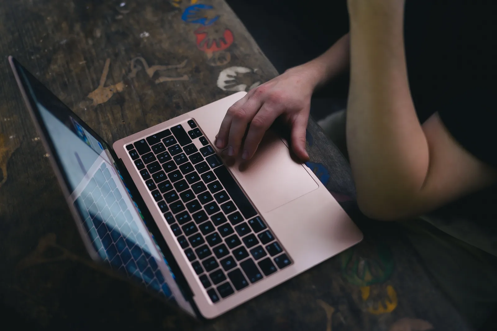 An adult uses a laptop on a rustic wooden desk, providing a cozy workspace vibe