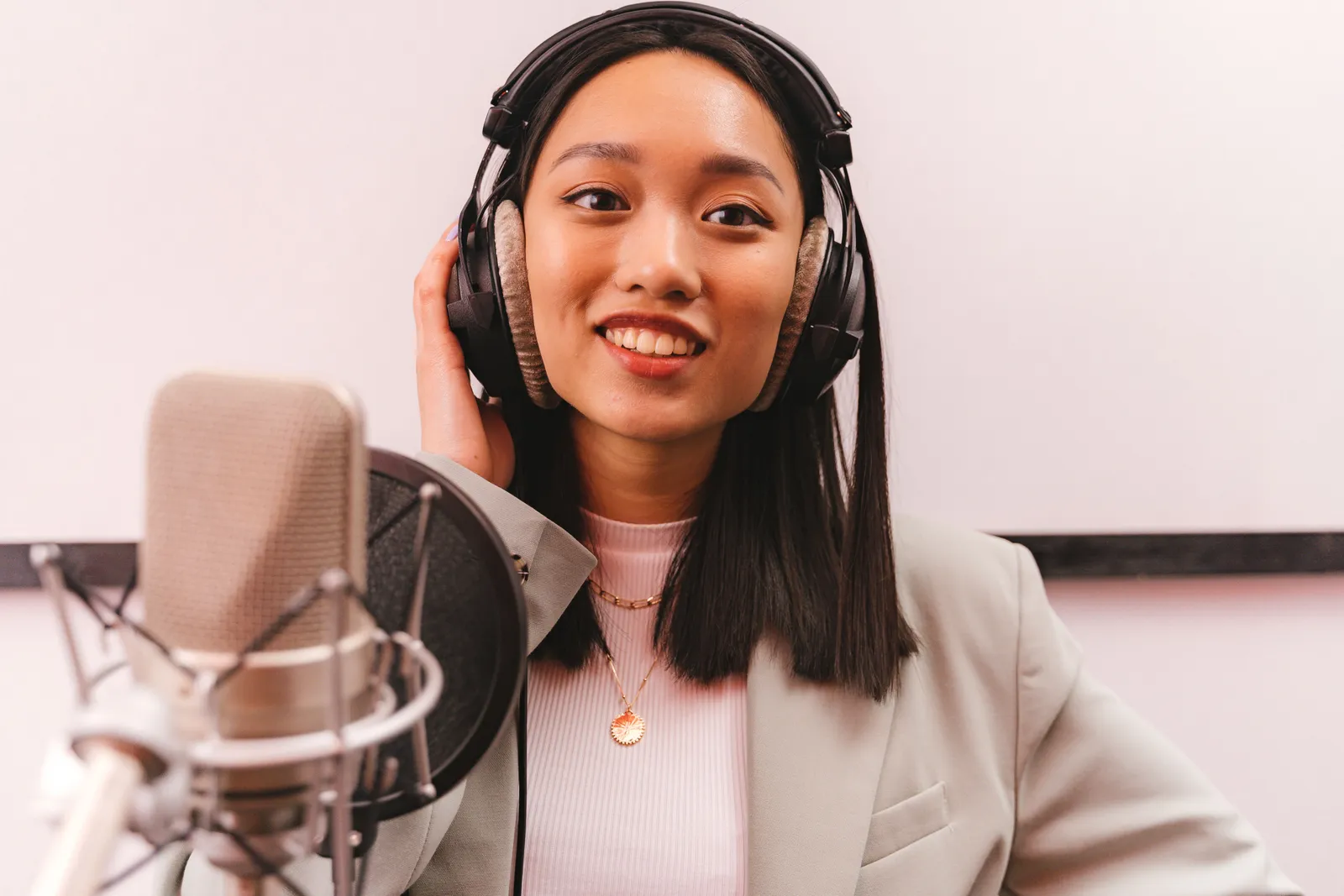 Smiling woman in a studio wearing headphones and speaking into a microphone for a podcast