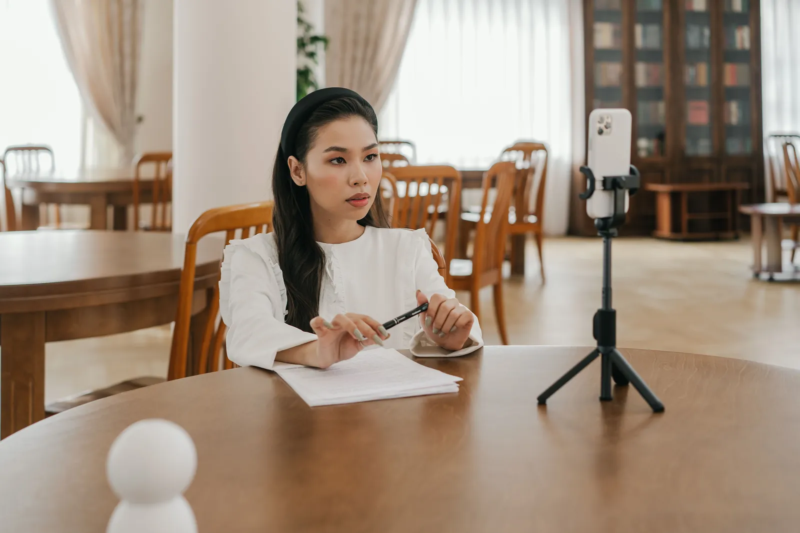 Woman using smartphone on tripod for online study in a library-like setting