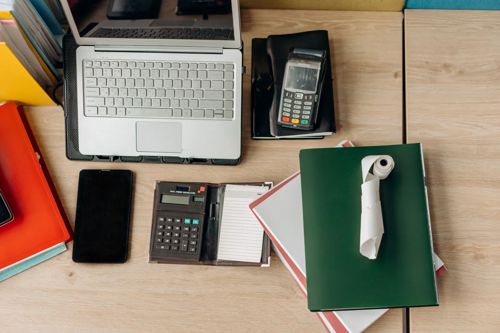 An organized office desk featuring a laptop, calculator, payment terminal, and documents