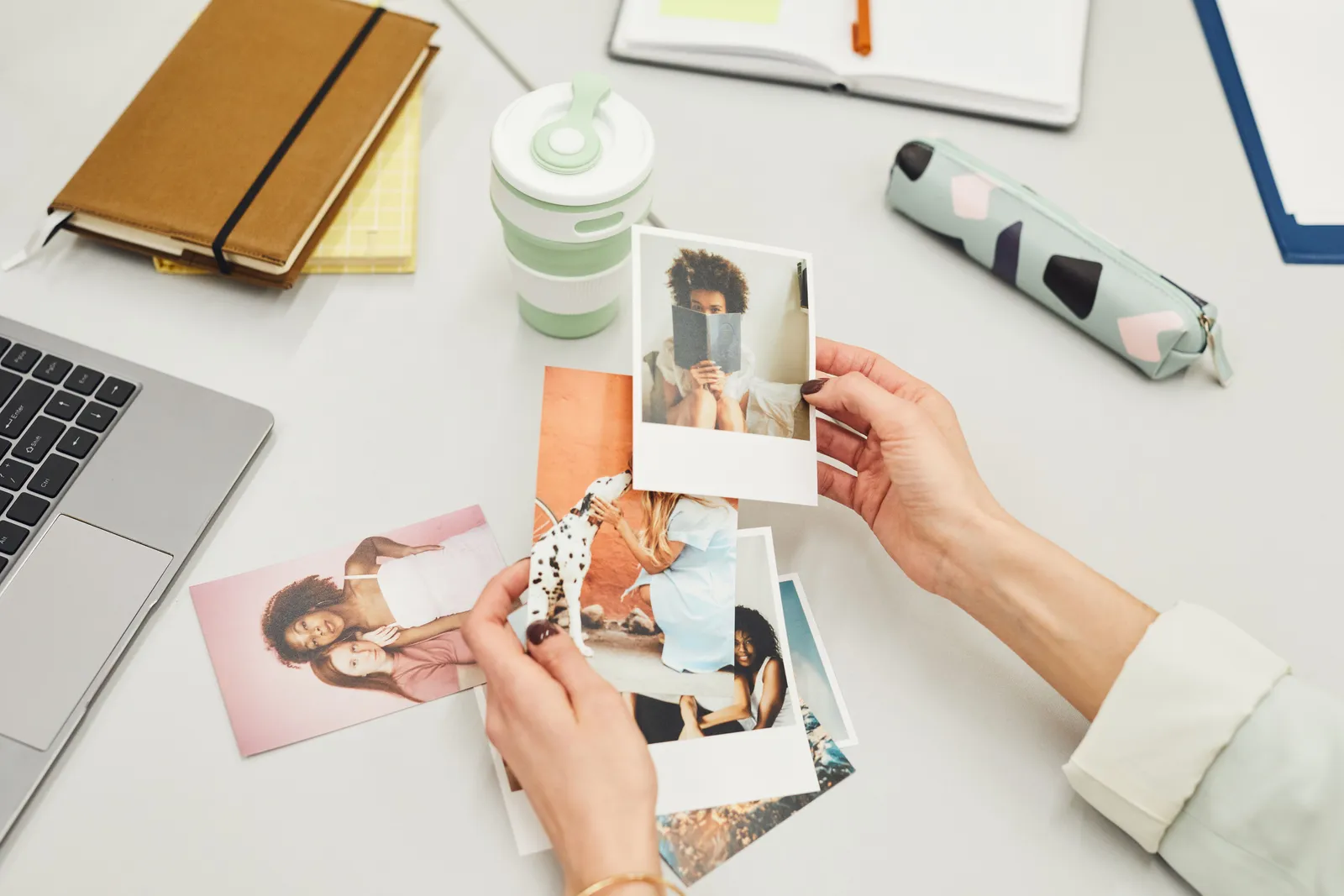 Close-up of hands holding polaroid photos on a creative workspace desk