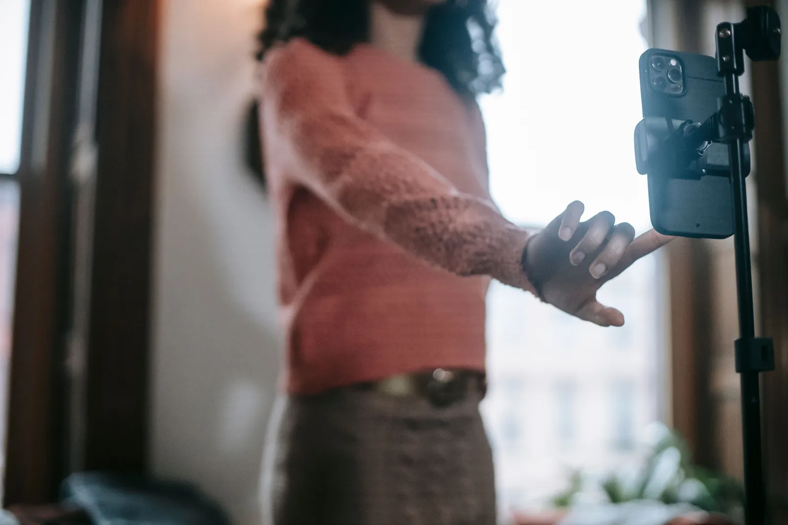 Crop unrecognizable female wearing orange sweater and beige knitted skirt taking selfie on mobile phone fixed on tripod