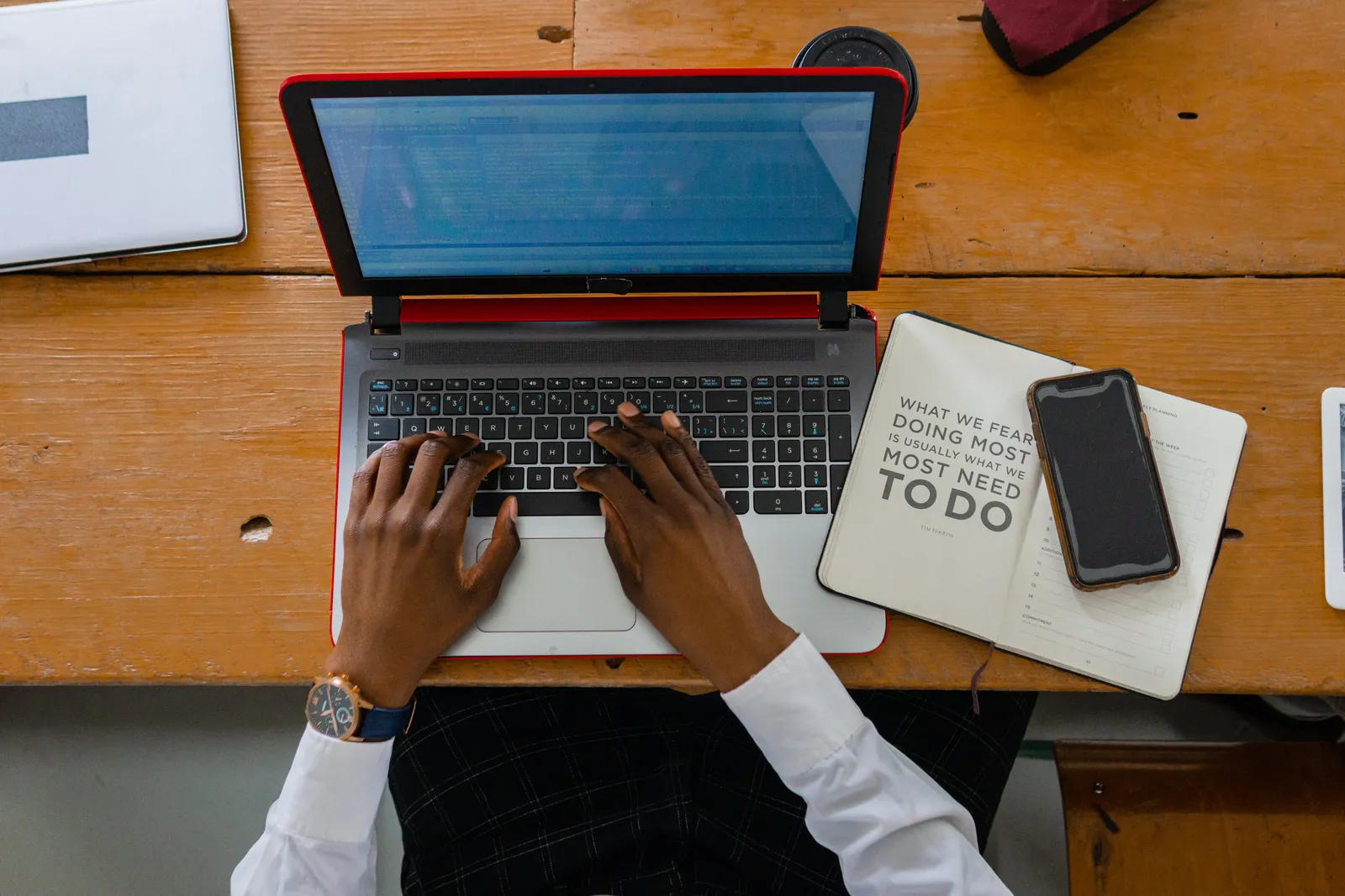 Person typing on a laptop with a notebook and smartphone on a wooden desk. Ideal for business or work themes