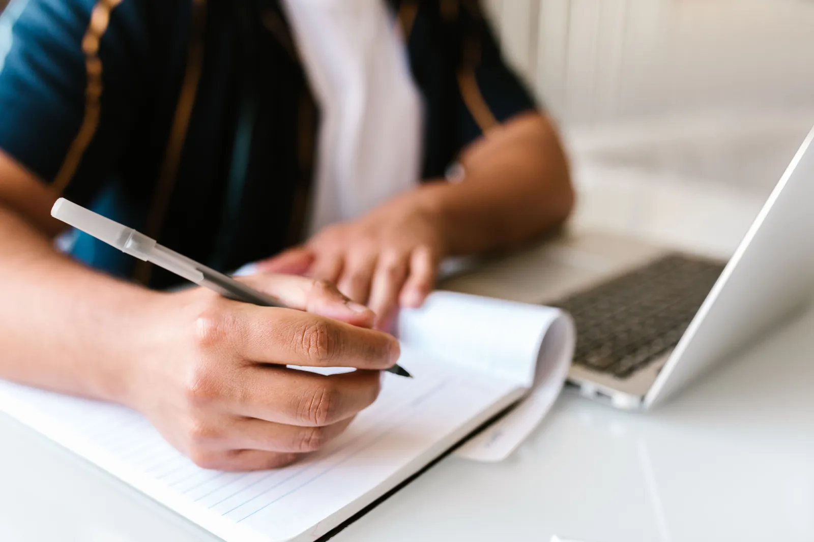 Focused image of a person writing in a notebook beside an open laptop, conveying productivity