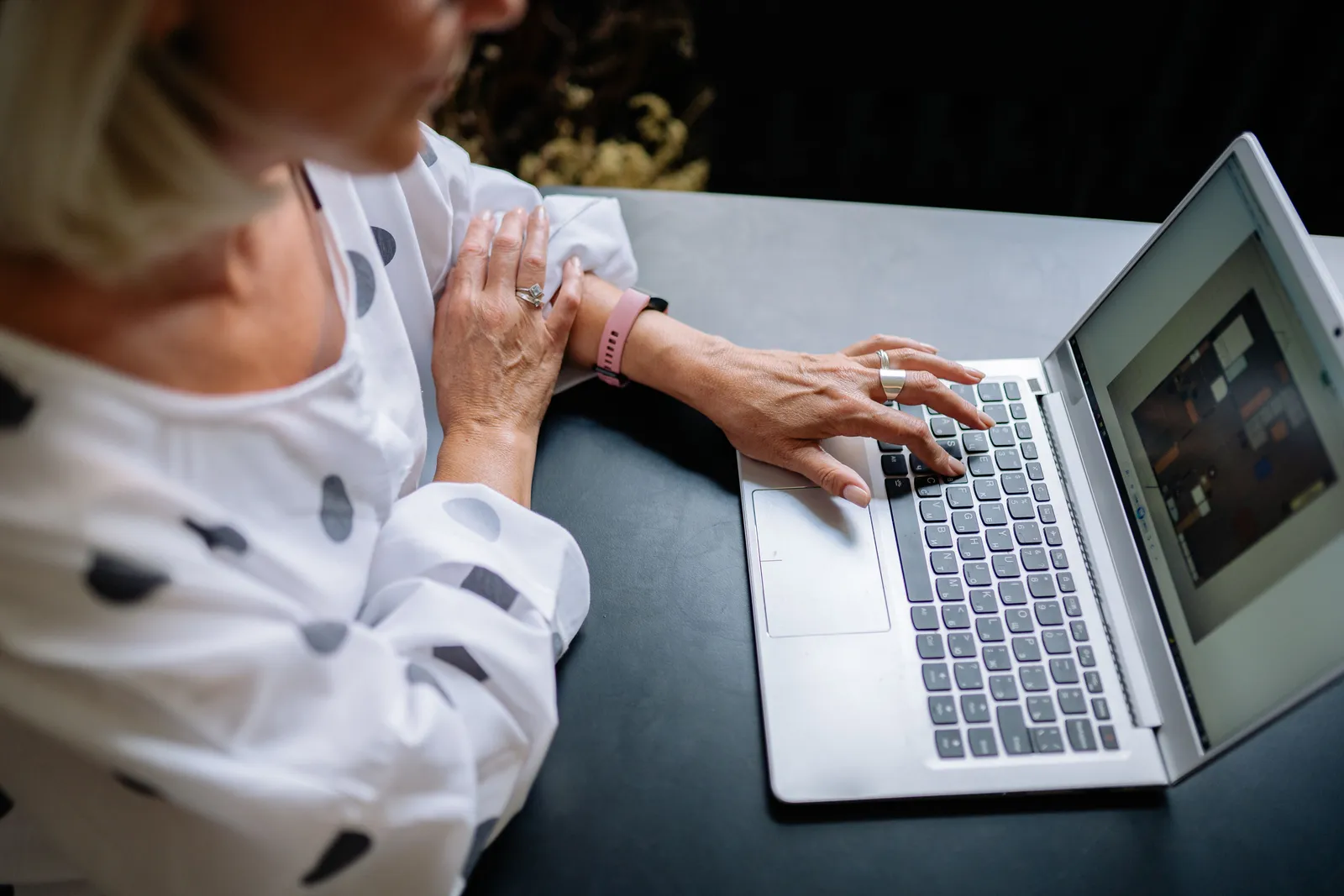 An adult using a laptop in a office space, focused on work. Polka dot attire indicates a casual style