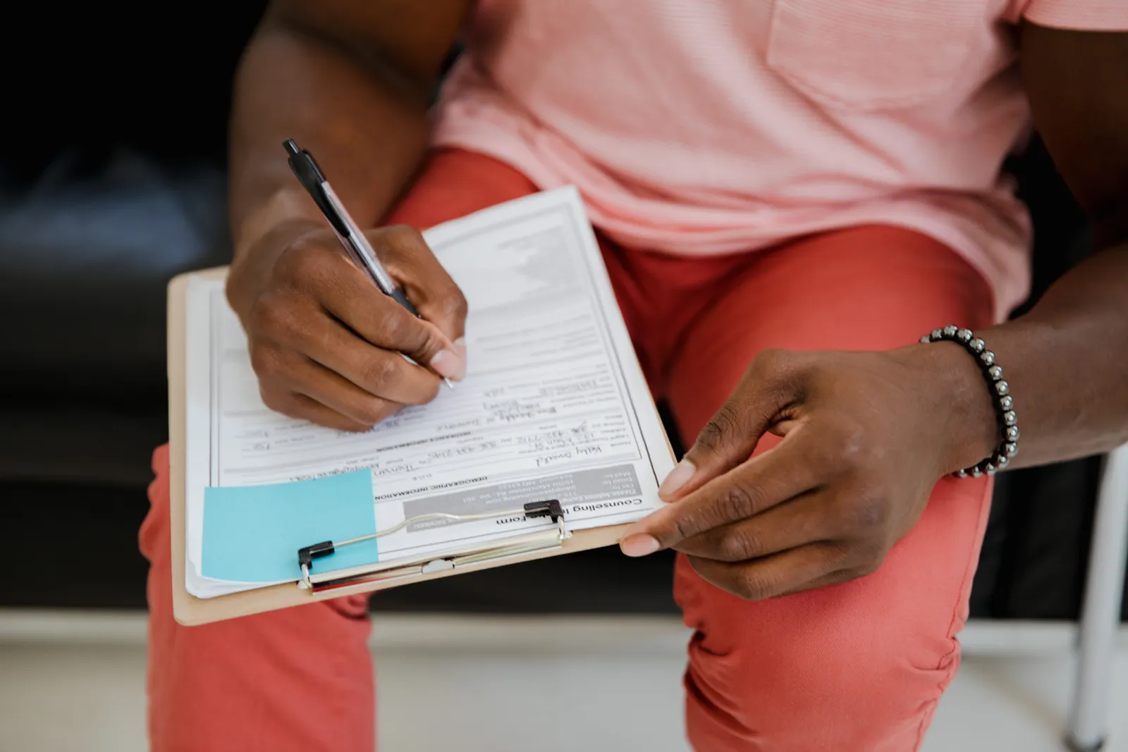 Close-up of a hand writing on a form with a pen attached to a clipboard