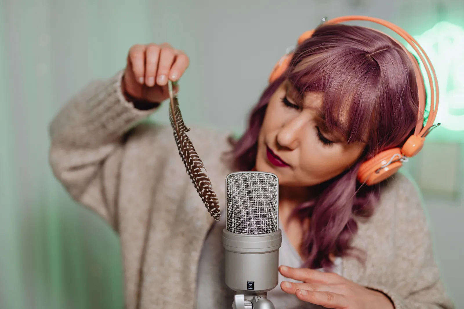 A woman uses a feather and microphone for ASMR recording in a cozy home studio