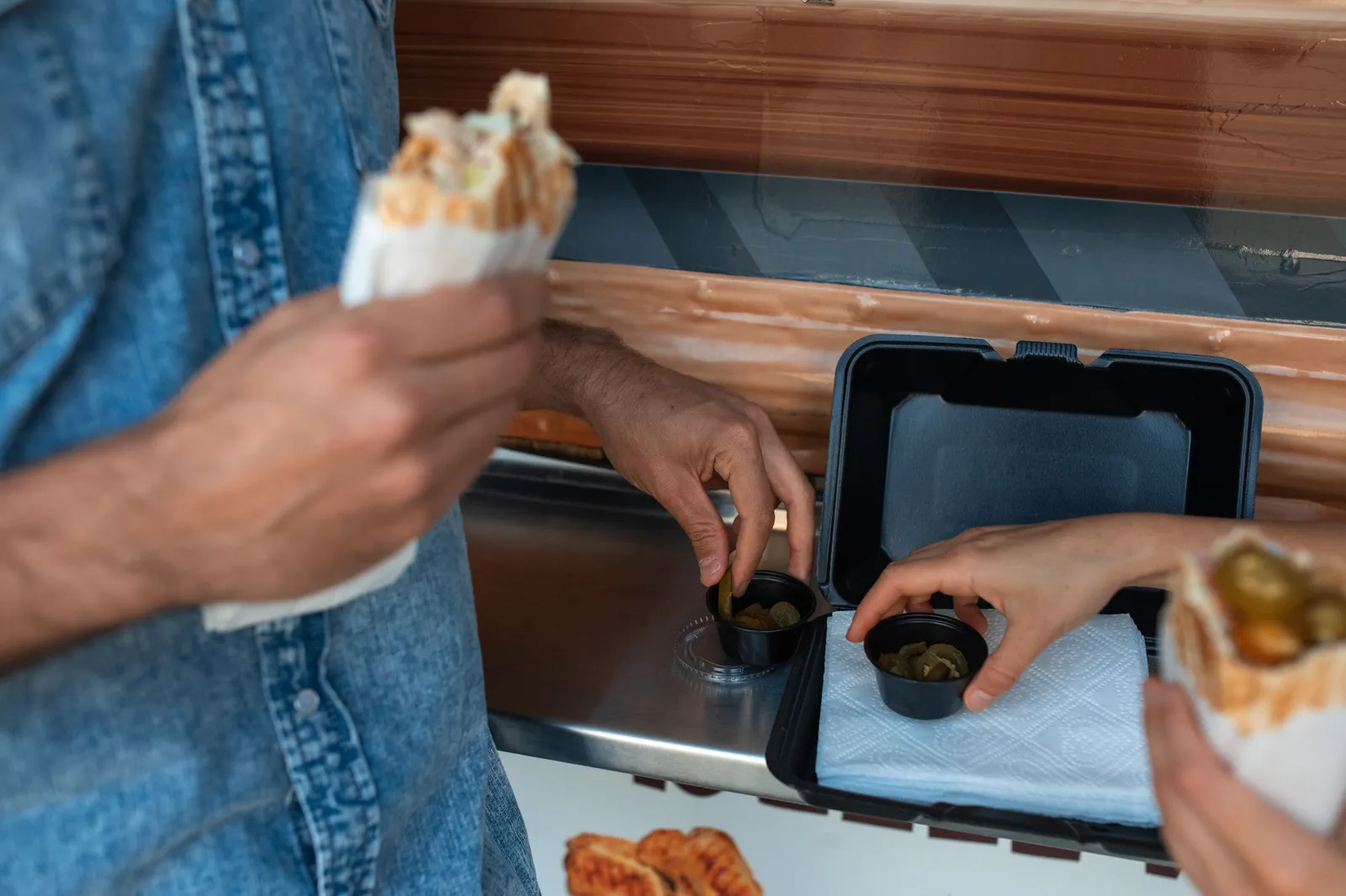 Hands holding shawarma and picking pickles at a food truck countertop