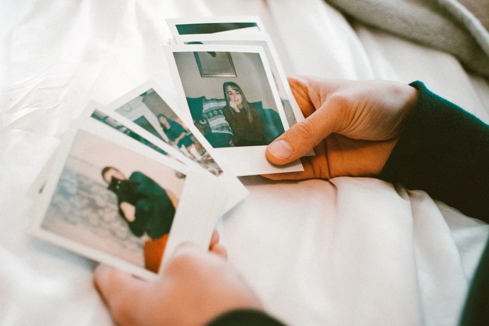 Hands gently holding a collection of printed photographs on a white bedspread