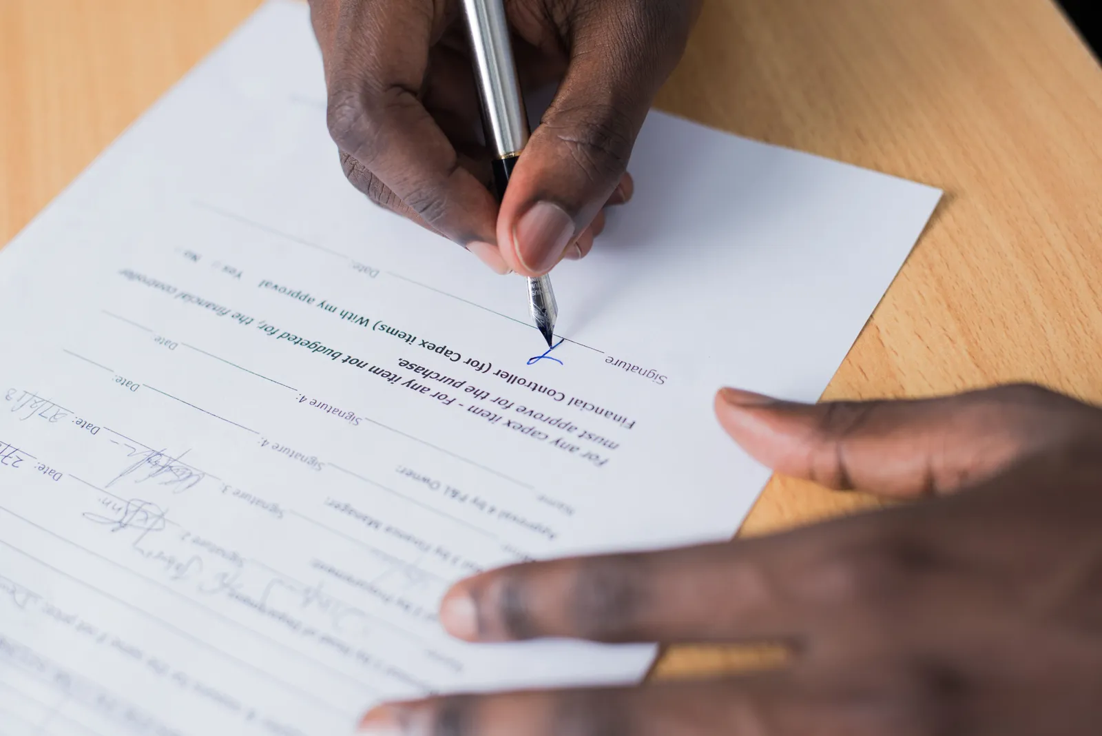 A close-up view of a person's hand signing a business contract on a desk with a pen