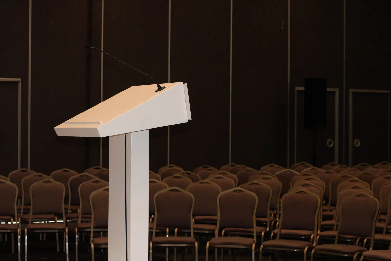An empty conference room setup with podium and rows of chairs, ready for an event